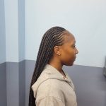 A woman with long braids standing in the bathroom, showcasing intricate hair braiding.